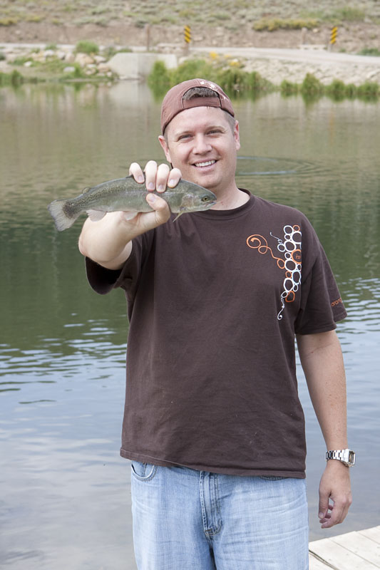 a man holds up a fish next to the water