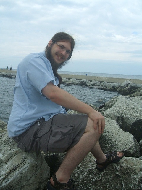 a bearded man sitting on rocks near the water
