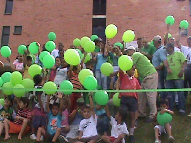 a group of people are sitting outside while some hold yellow and green balloons