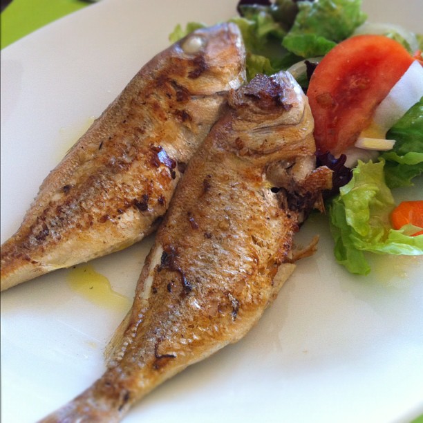 two fried fish are on a plate with some salad