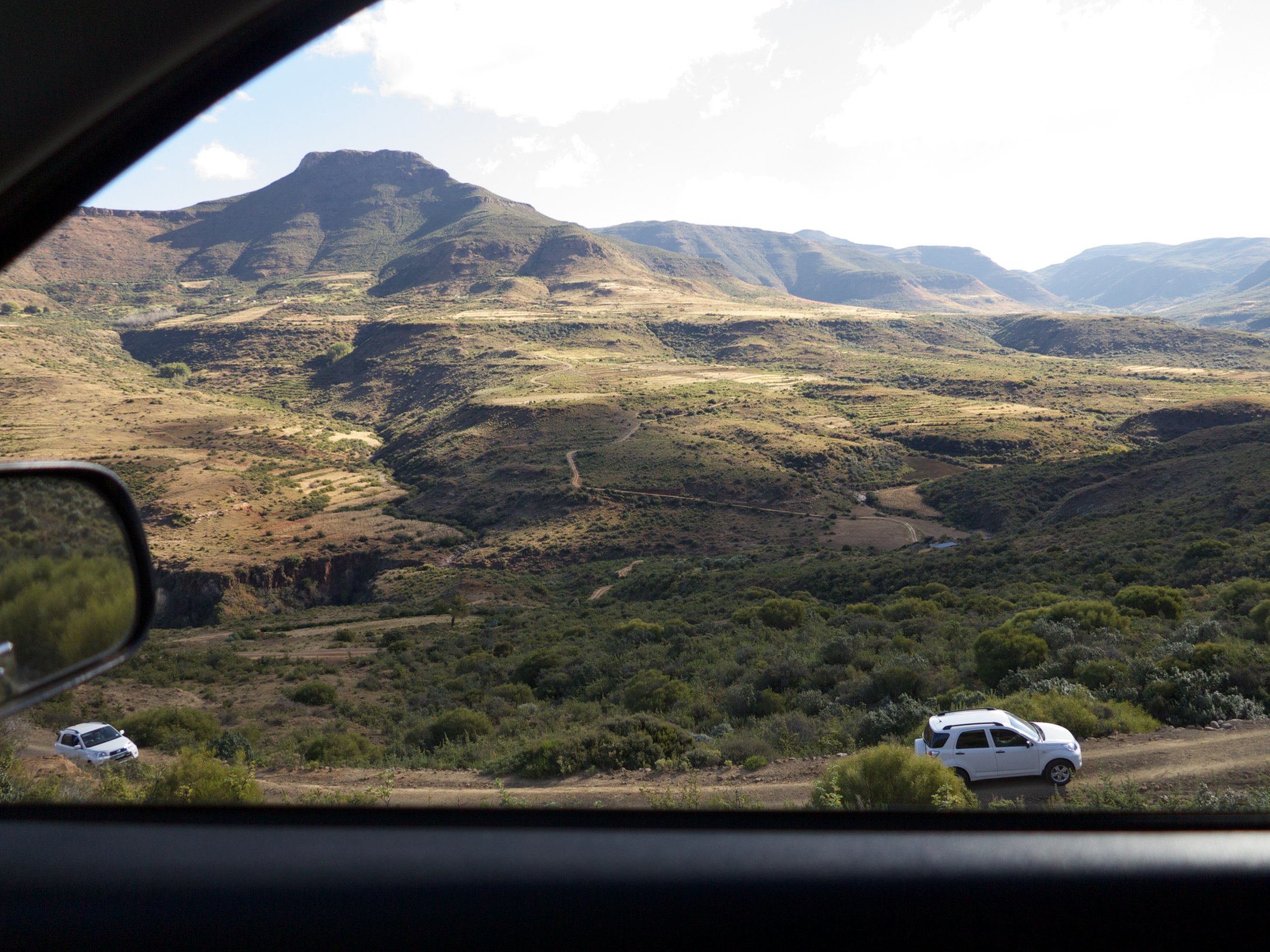 some cars on the side of a hill with mountains