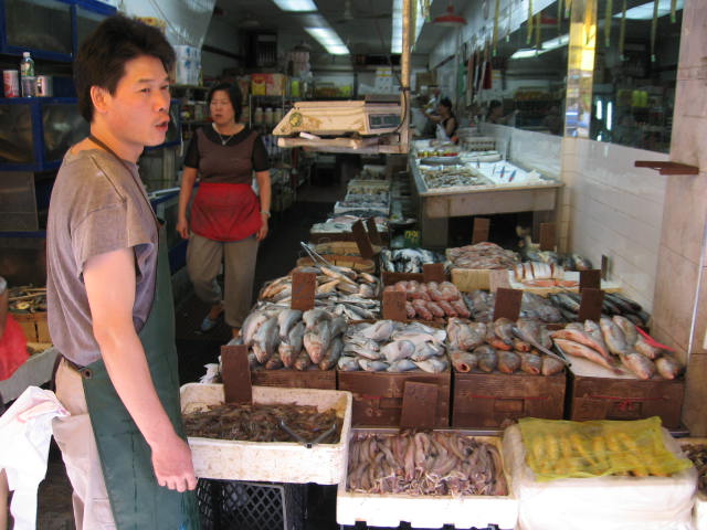 a man standing in a market area next to a large tray full of fish