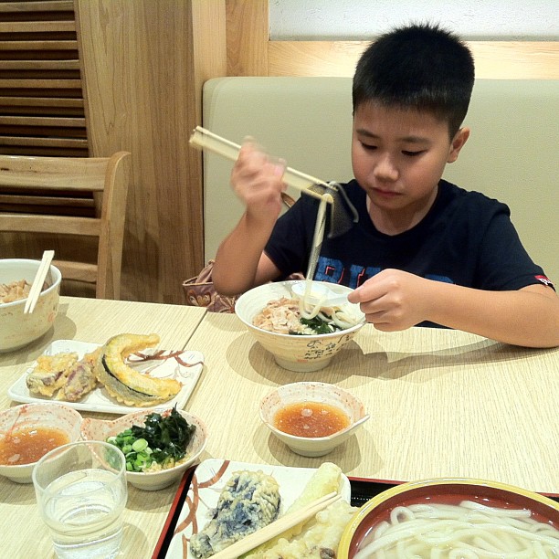 a boy is sitting at a table eating sushi