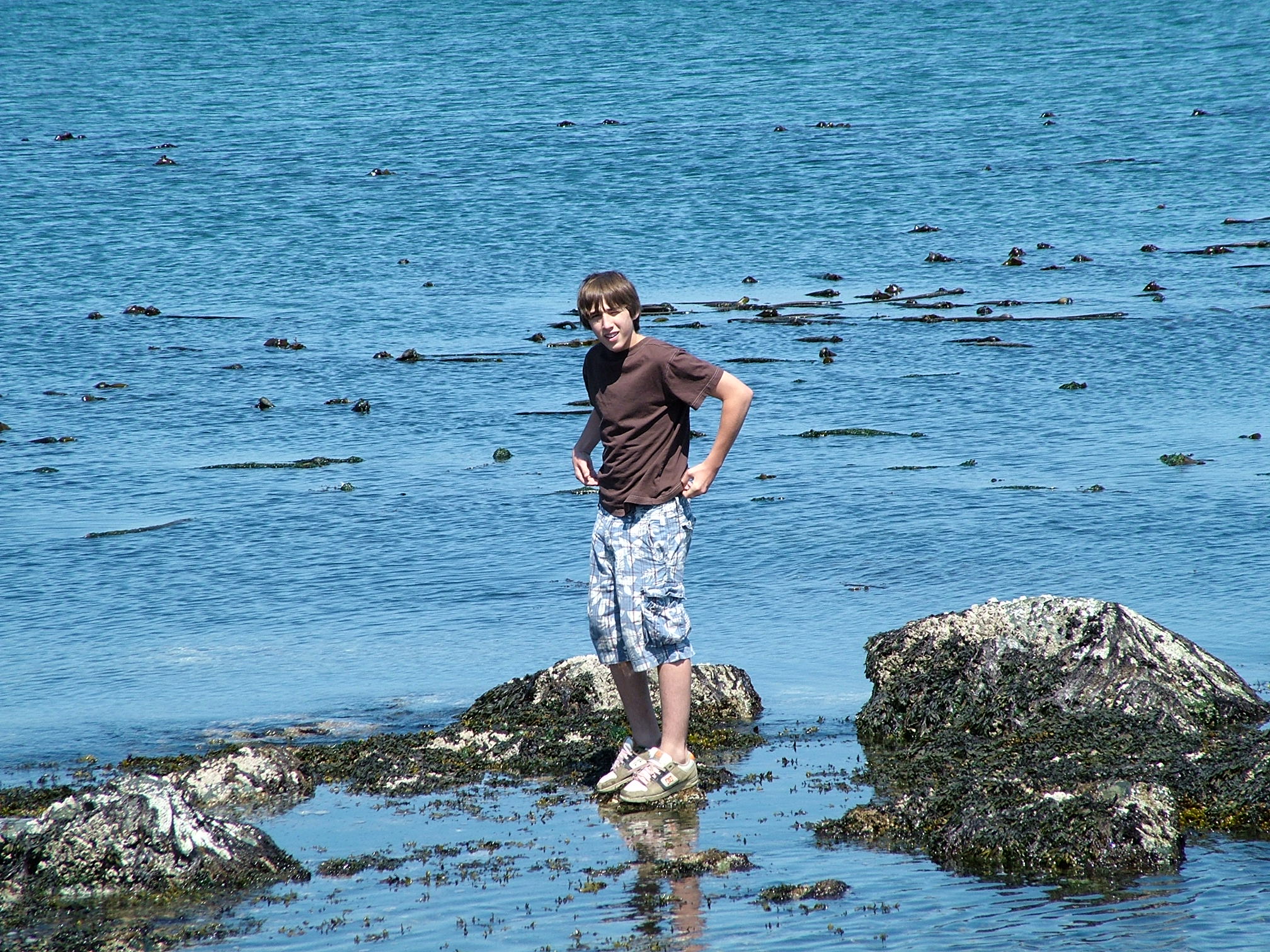 a boy is standing in shallow water near rocky shore