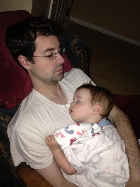a man holds his small baby while he sleeps