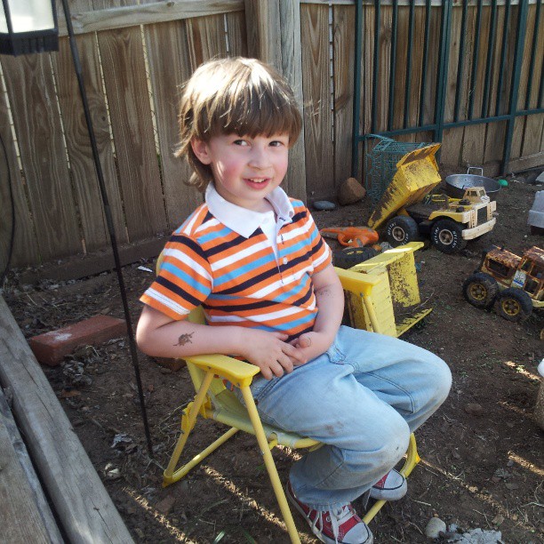a little boy sitting on a chair and toys in the back yard