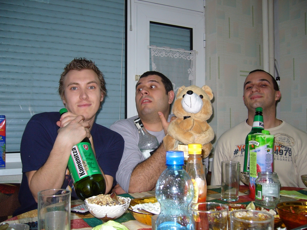 three men sit at a table with drinks and stuffed animals