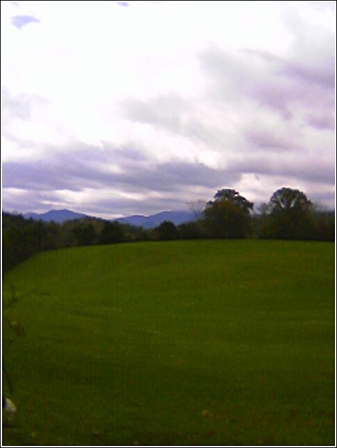 a green field and some mountains under a cloudy sky