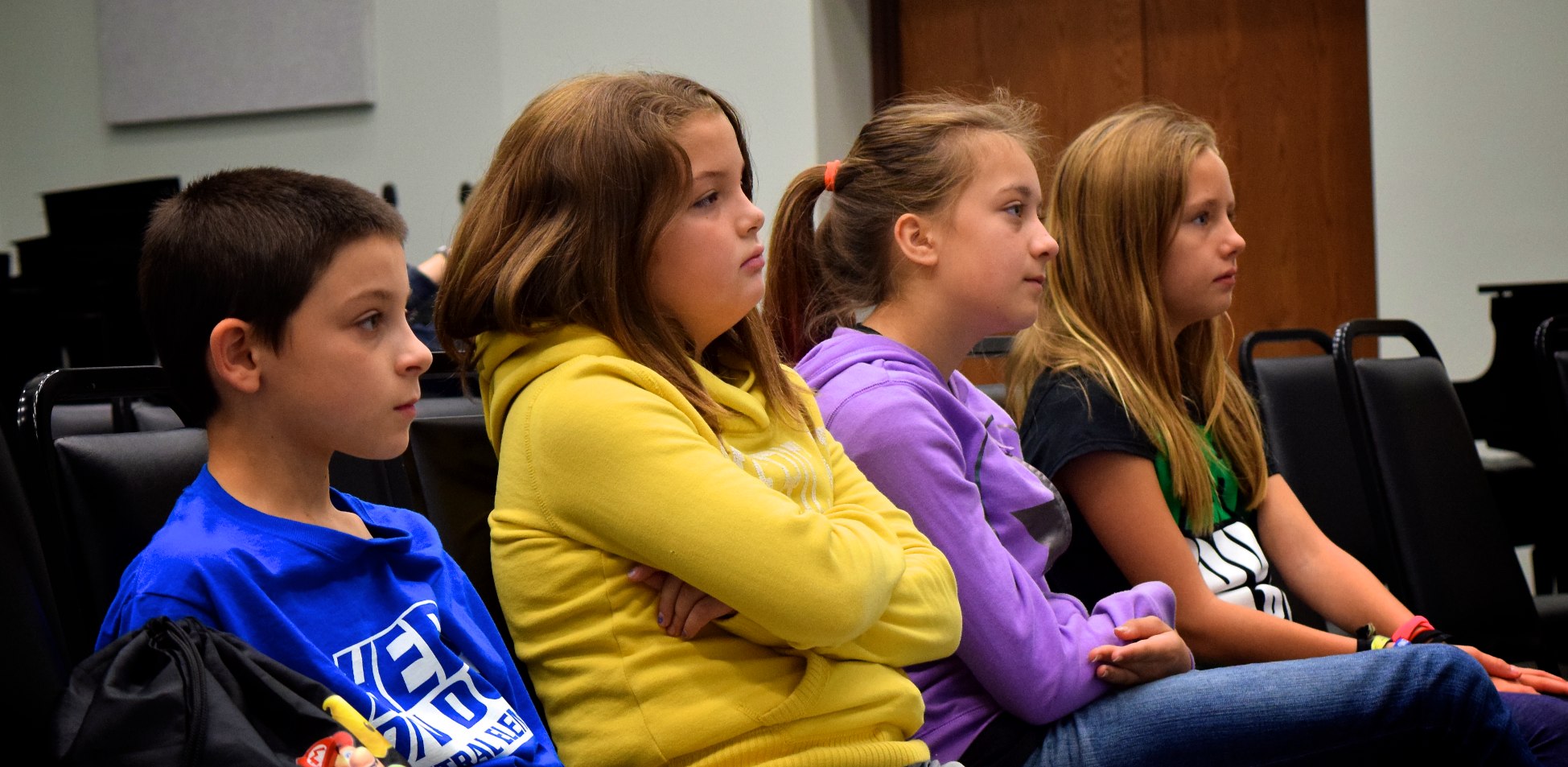 group of children in a lecture hall with their arms crossed