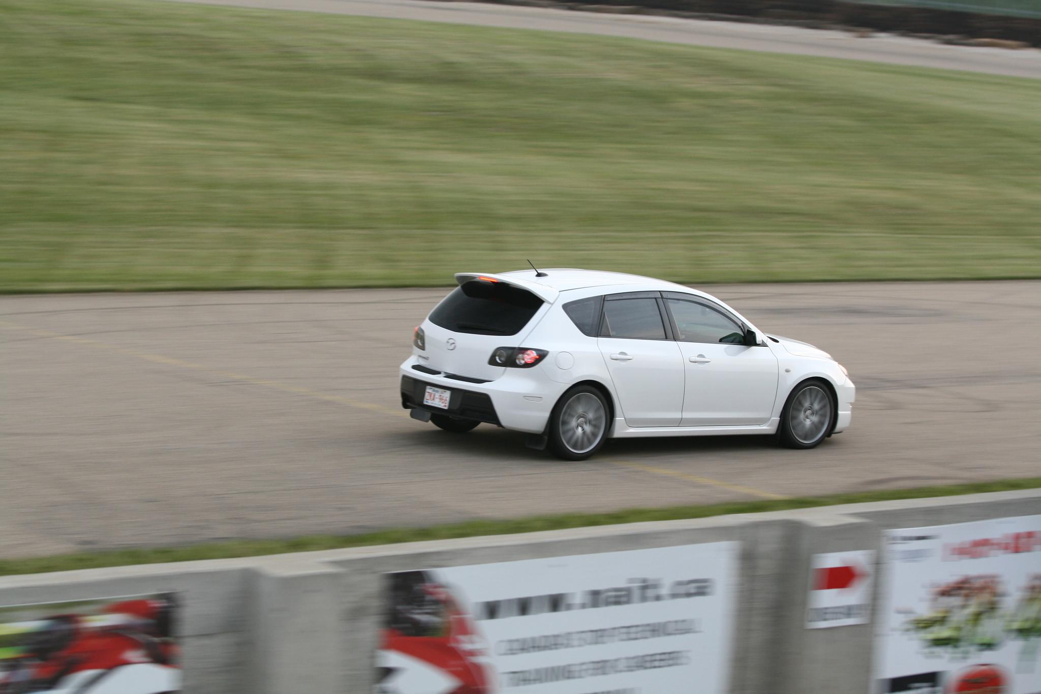 a small white car on the road near a grass covered field