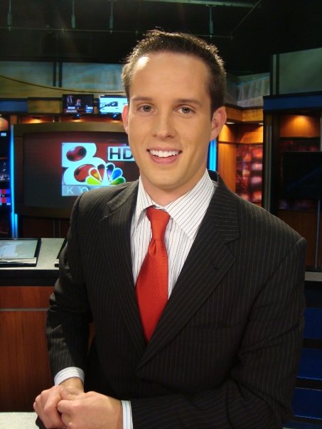 man in business suit in news studio with two televisions