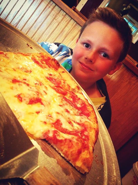 the young child is enjoying his large piece of pizza