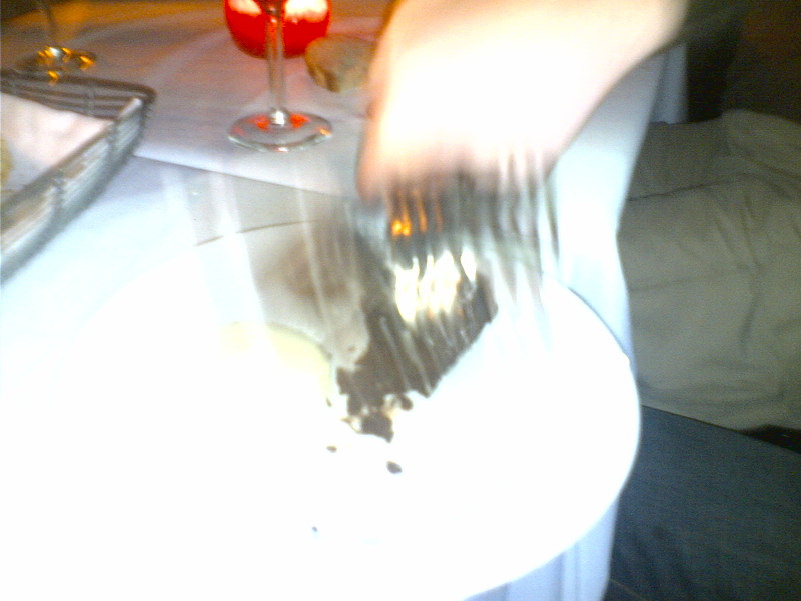 someone holding a fork with cake sitting on top of a table