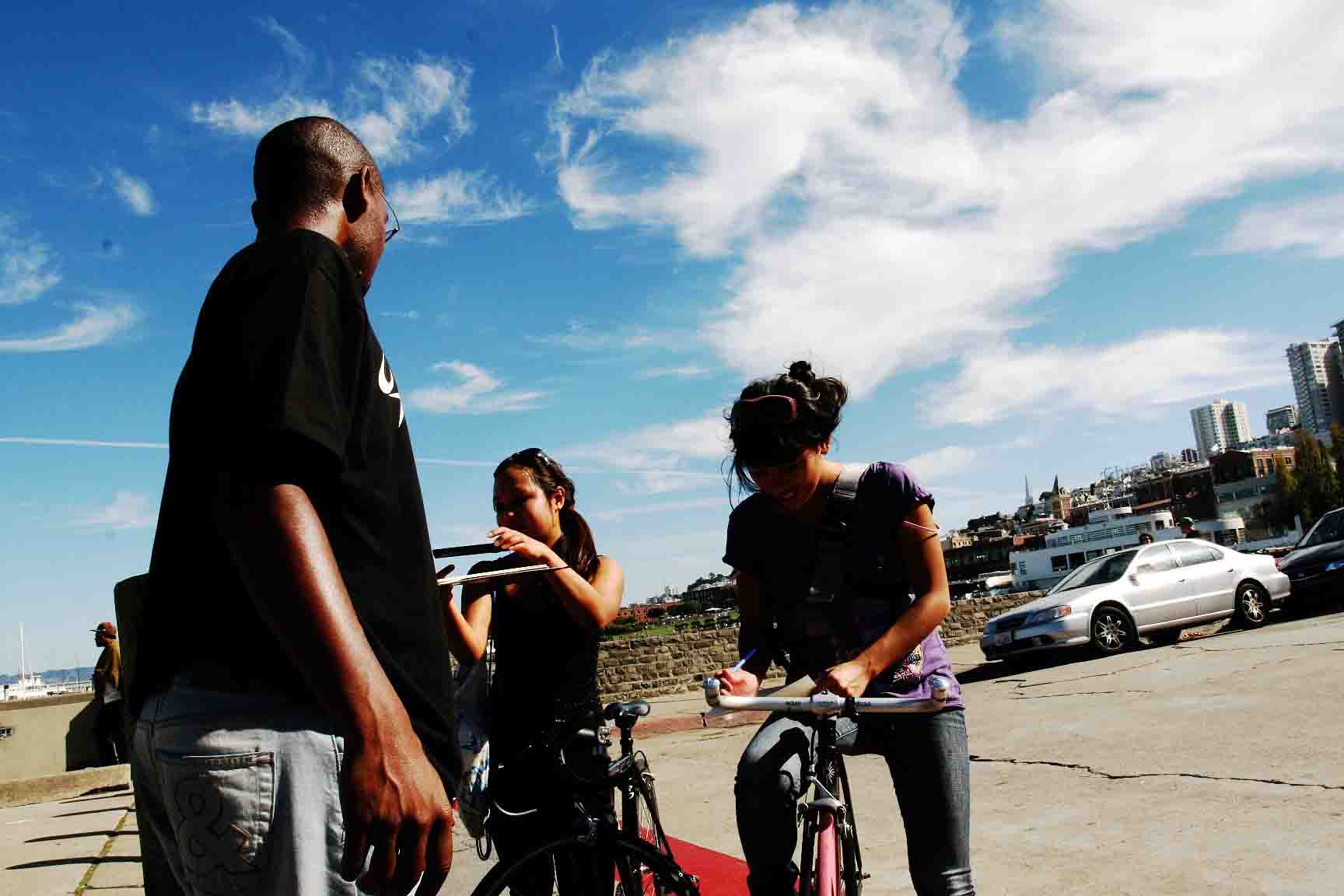 three people waiting on a sidewalk to ride bikes