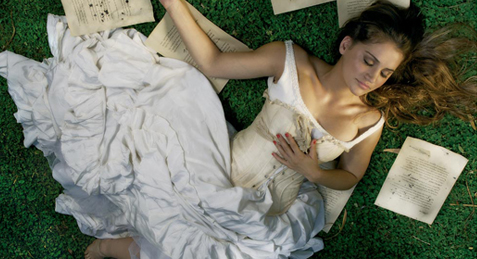 an overhead s of a woman laying down on the grass with lots of old documents on her lap