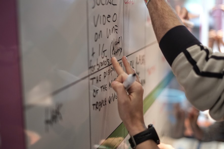 a person writes on a white board next to people