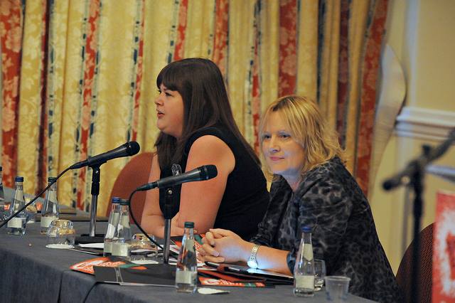 two women sitting at a table together with microphones