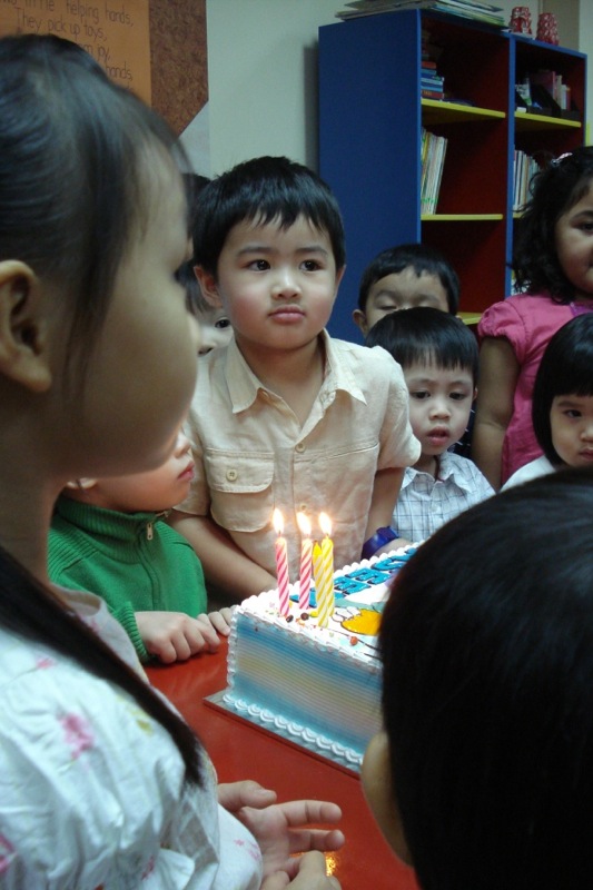 children are looking at a birthday cake with candles