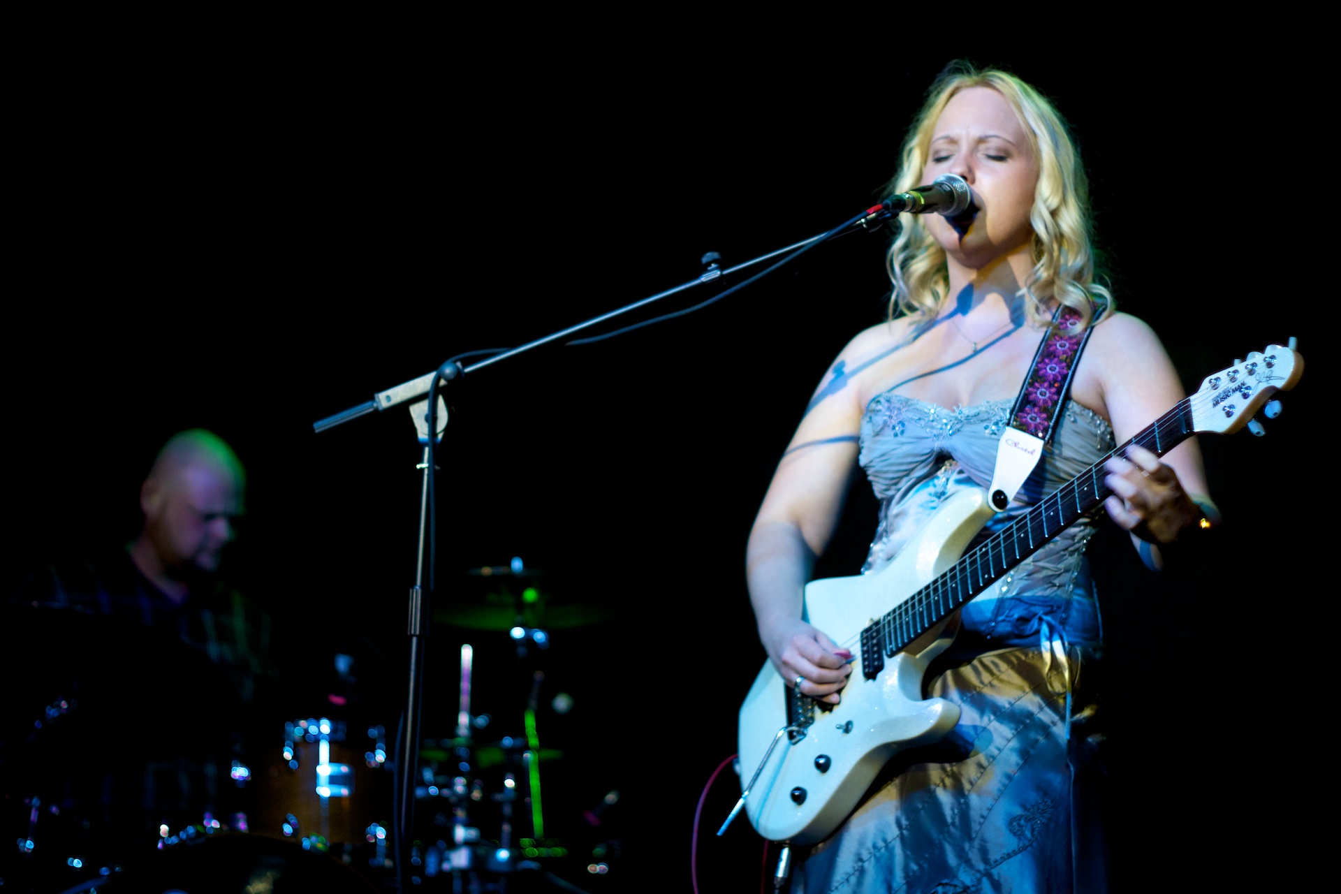 woman with long blonde hair playing guitar in front of microphone