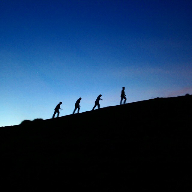 a line of four people walking on a hill under a blue sky