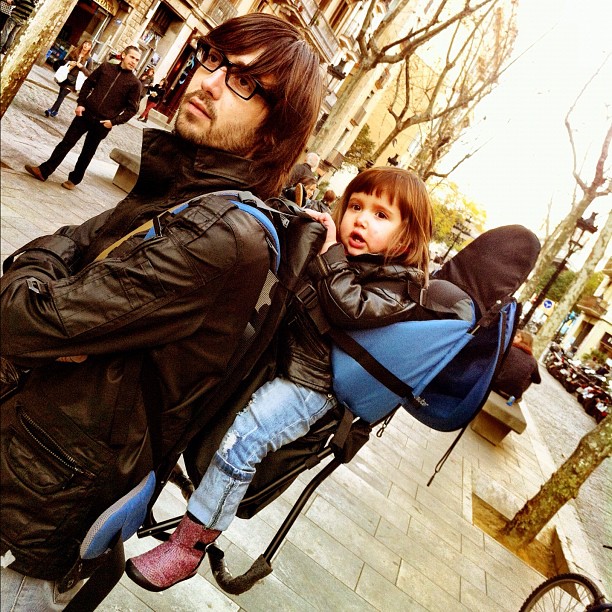 a man with glasses is holding a small child in his backpack
