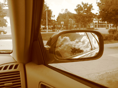 the rear view mirror of a vehicle shows clouds in the air