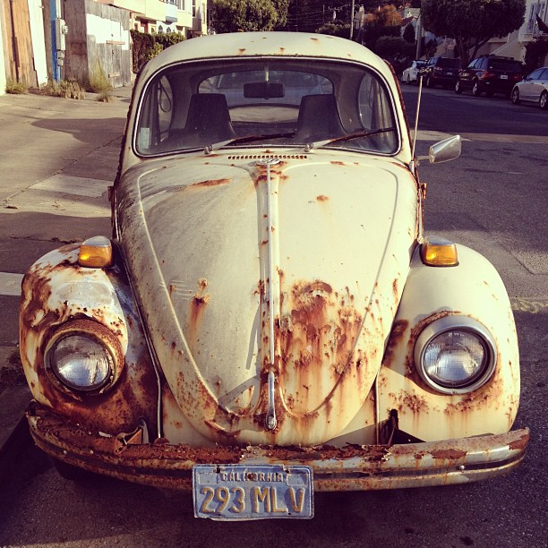 a white, rusted old beetle in the street
