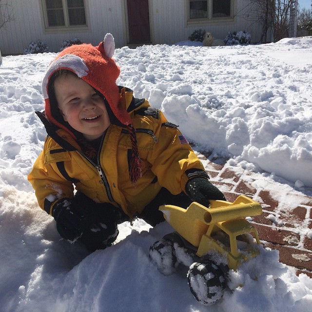 a baby in the snow smiling as he plays with his toy truck