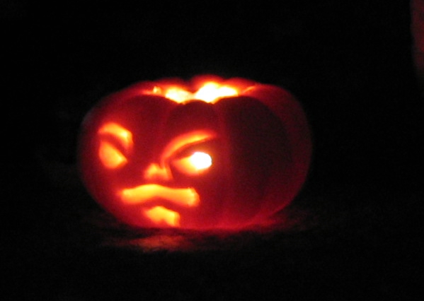 the glowing carved pumpkin shows it's teeth and a frown