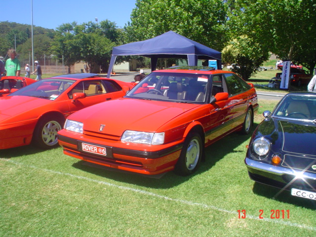 two red cars are parked on the grass near other cars