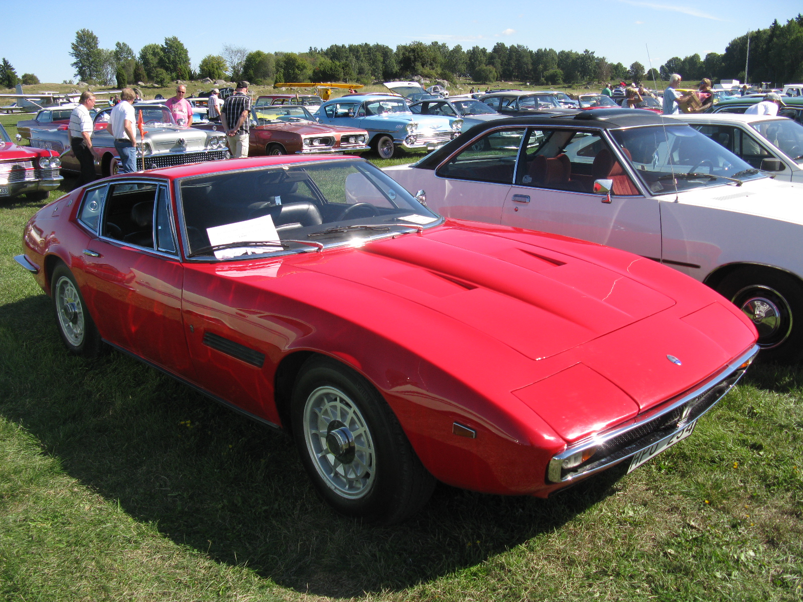 a red car parked in the grass with people around it