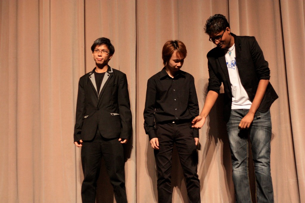 three young men standing on stage in front of a curtain