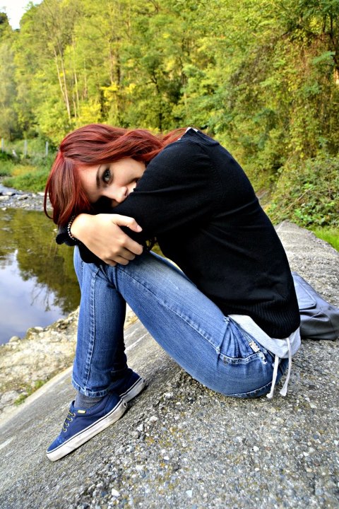 a young woman poses for the camera as she is crouched over by a creek