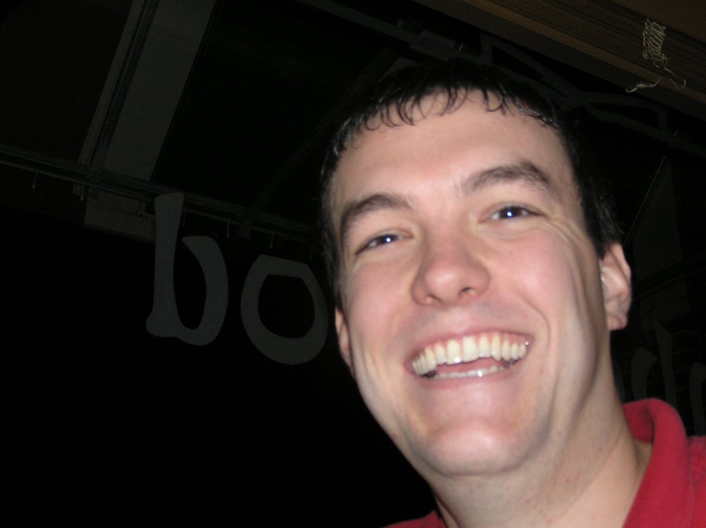 a man smiles into the camera wearing a red shirt