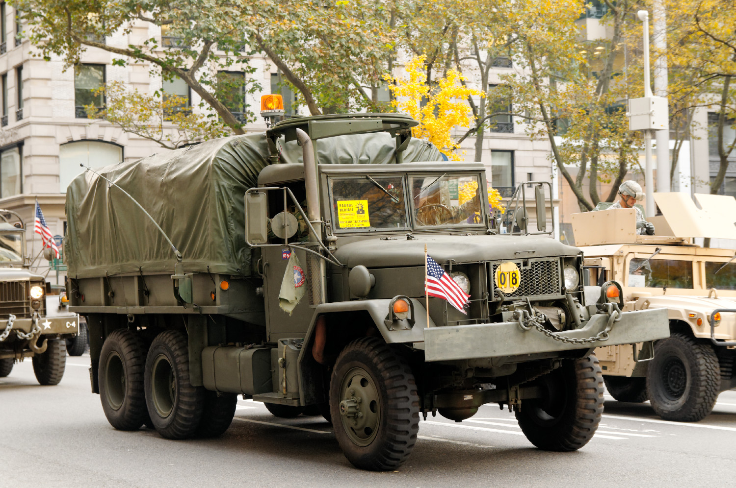 an army green truck with two trucks driving down the street