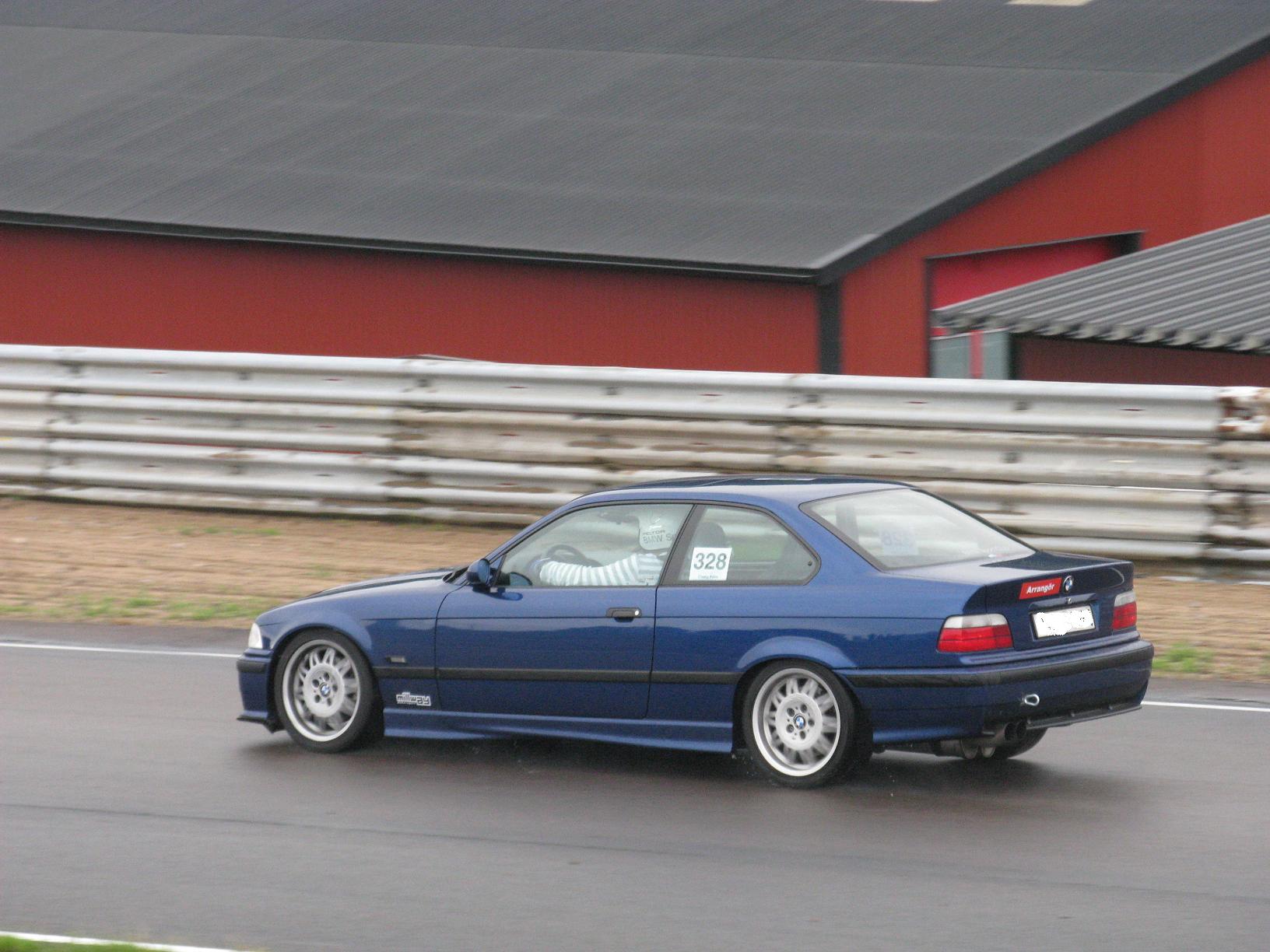 a blue car driving down a street past a barn