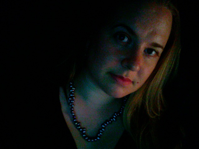 woman with beaded necklace, black shirt and dark background