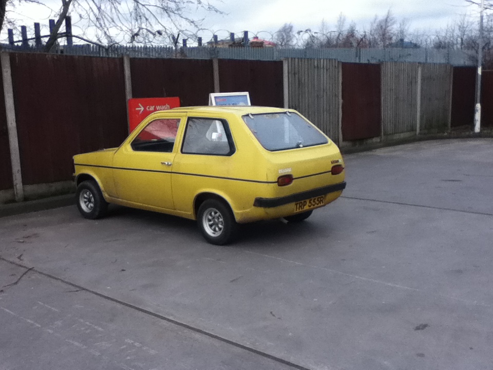 an old yellow car parked in a parking lot