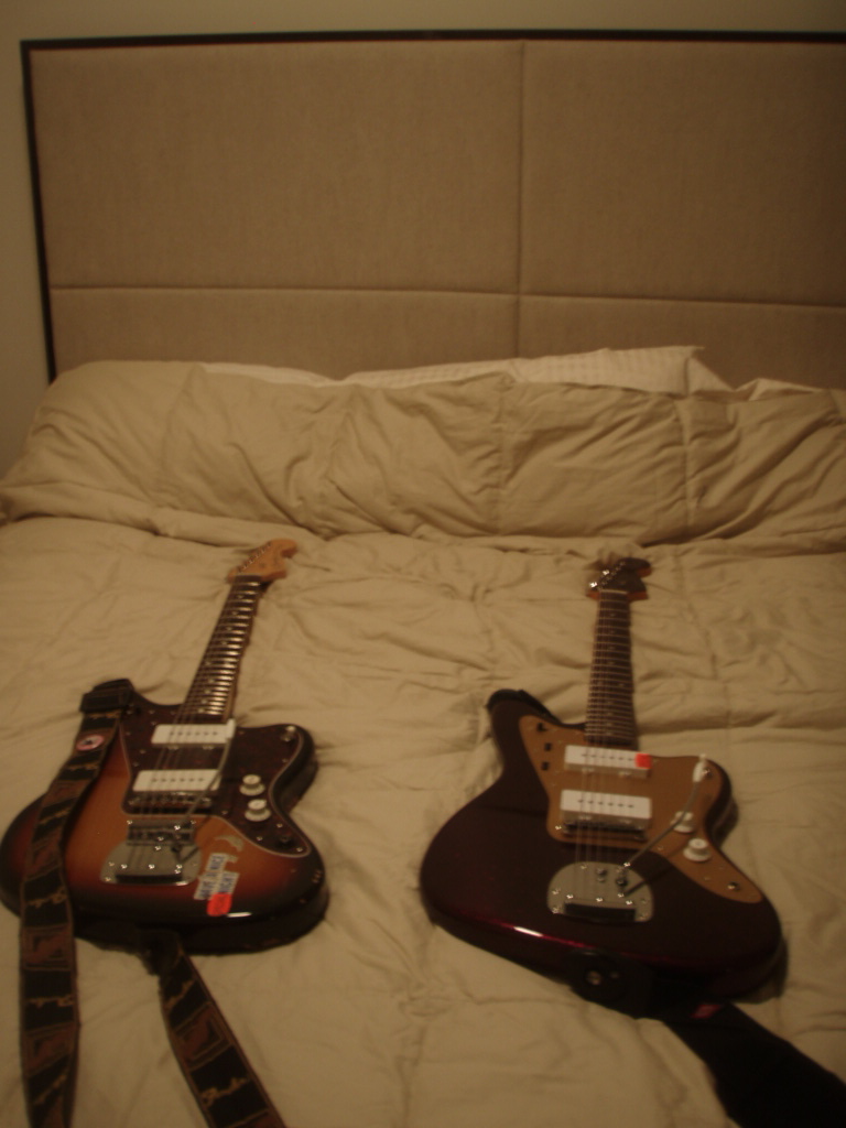 two guitars are laying on a bed with their heads resting in one