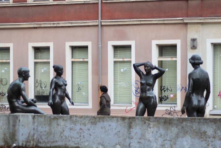 three bronze sculptures of three women in front of a building