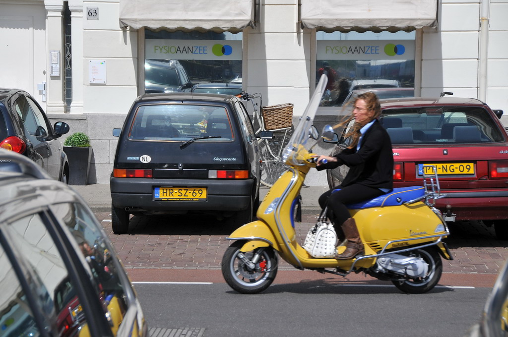 a woman in a business suit and heels rides on a moped