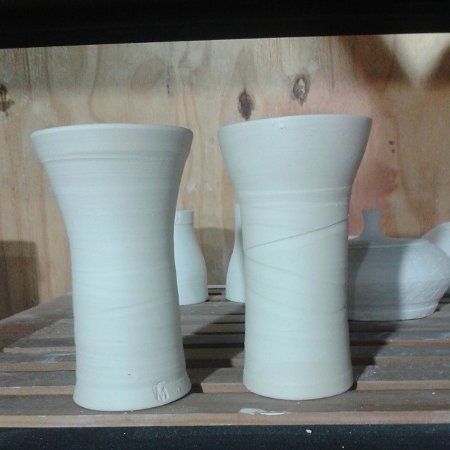 two small white vases are on a rack