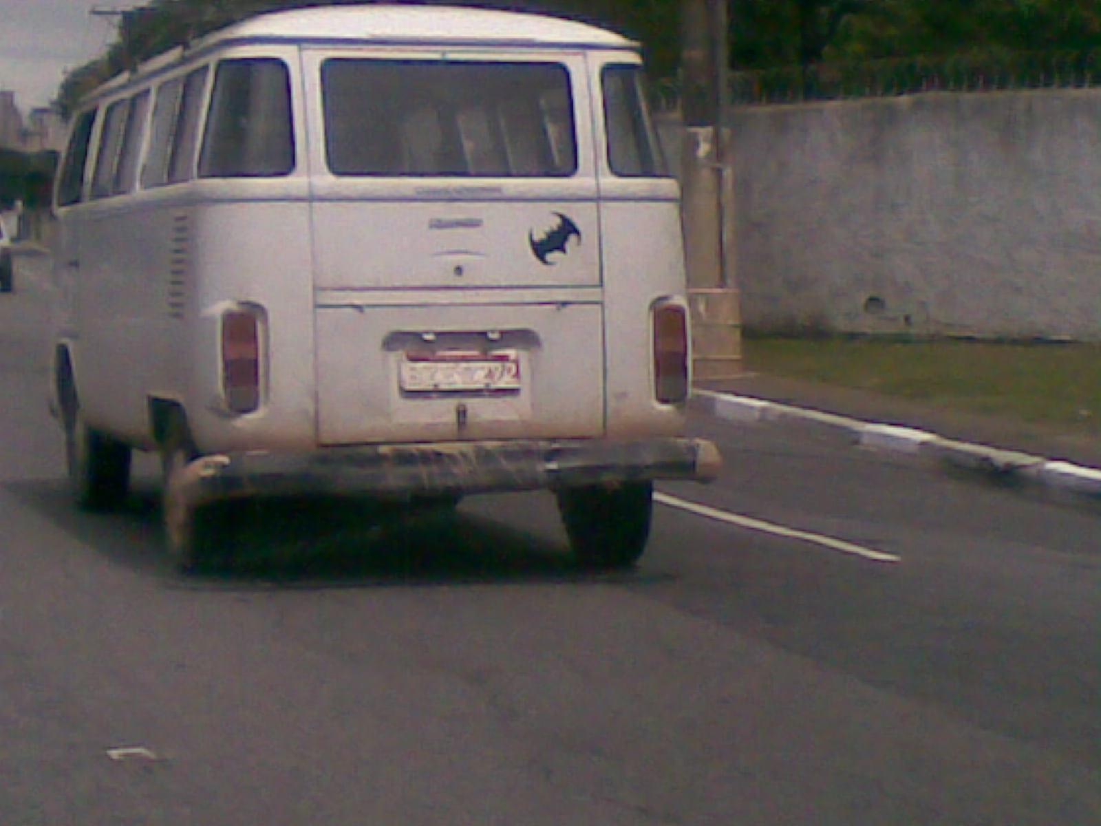 an old van driving down a street past a brick wall