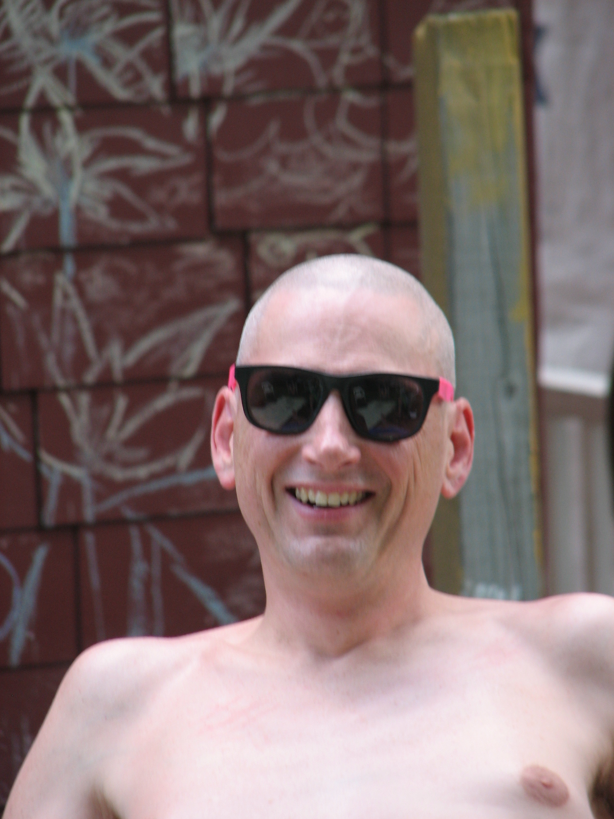 a shirtless man standing by a wall wearing sunglasses