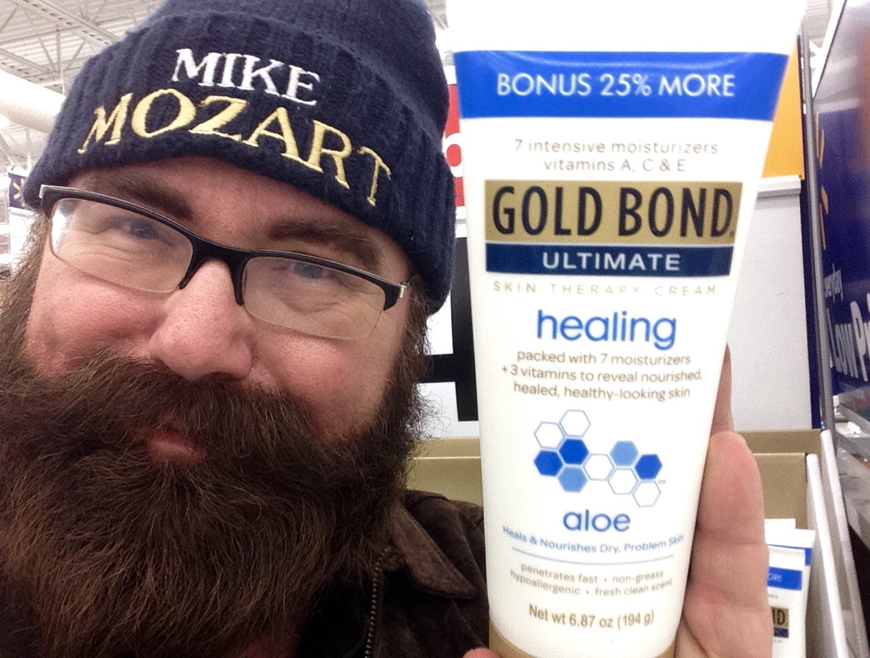 a man with glasses and a hat holds up a tube of gold bond