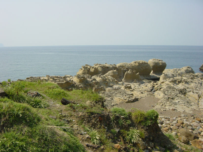 two rocks on the edge of a rocky outcropping with sea in the background