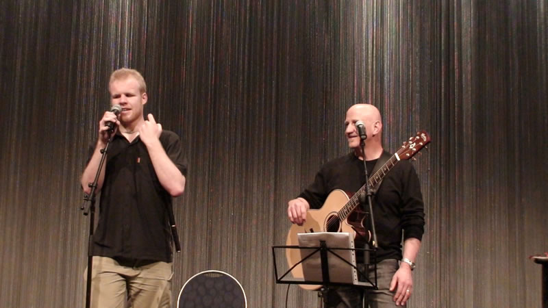 two men singing while standing next to each other with one holding a guitar