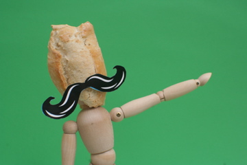 the small person with a fake mustache has some sort of bread in his hand