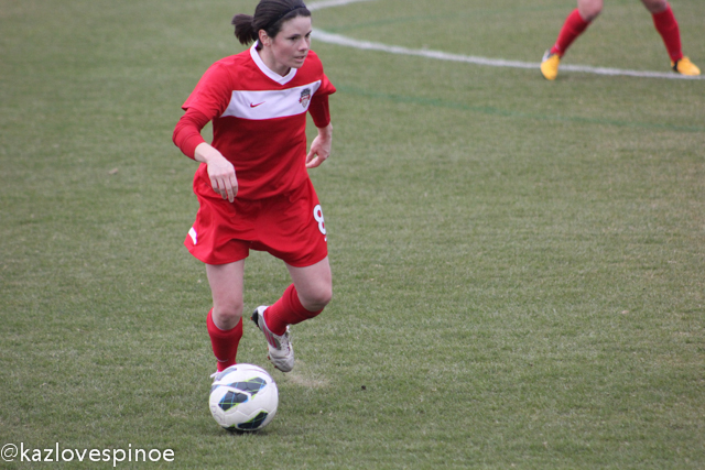 the girl is wearing red while kicking the ball