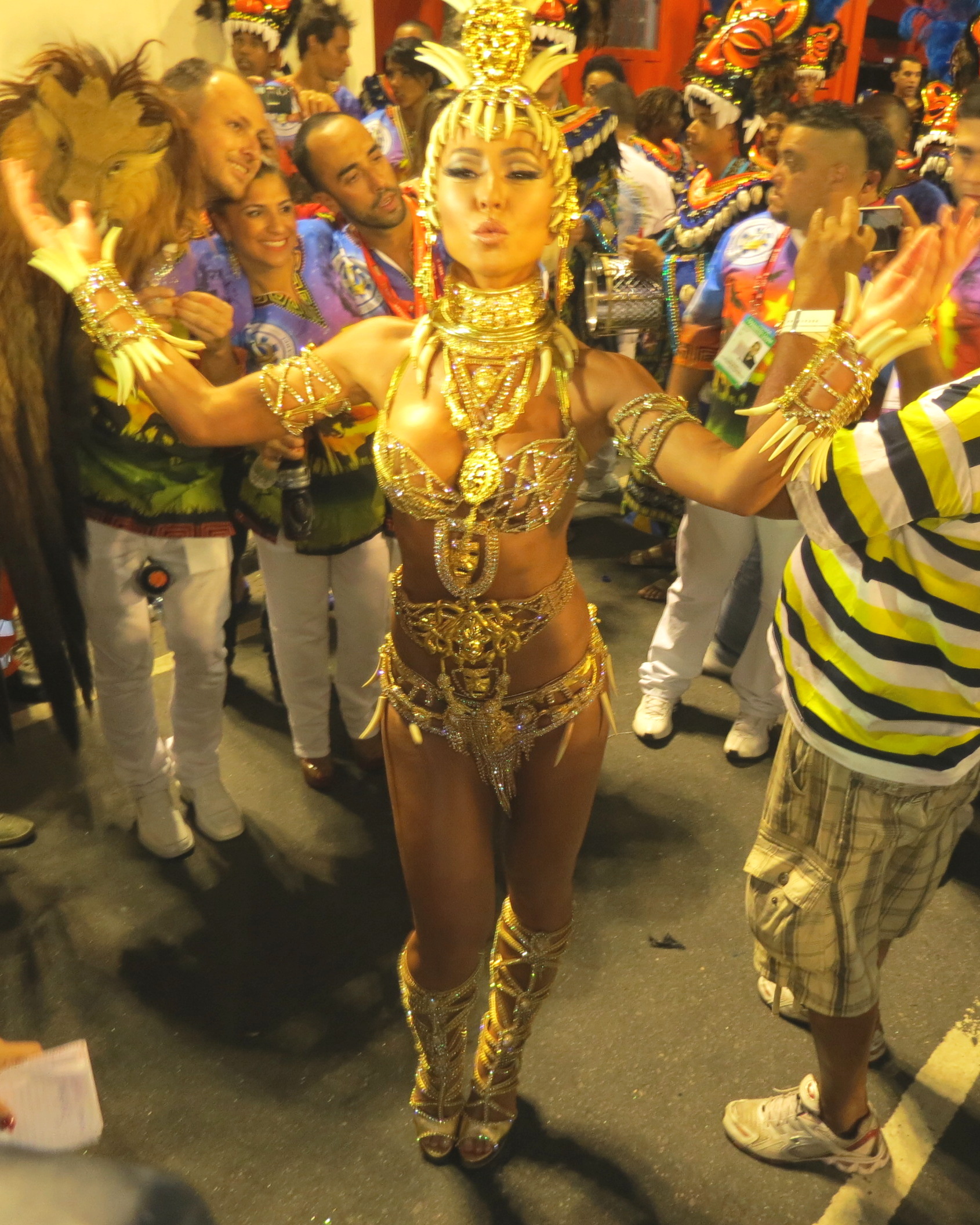 a woman wearing gold and costume stands in the middle of a crowd